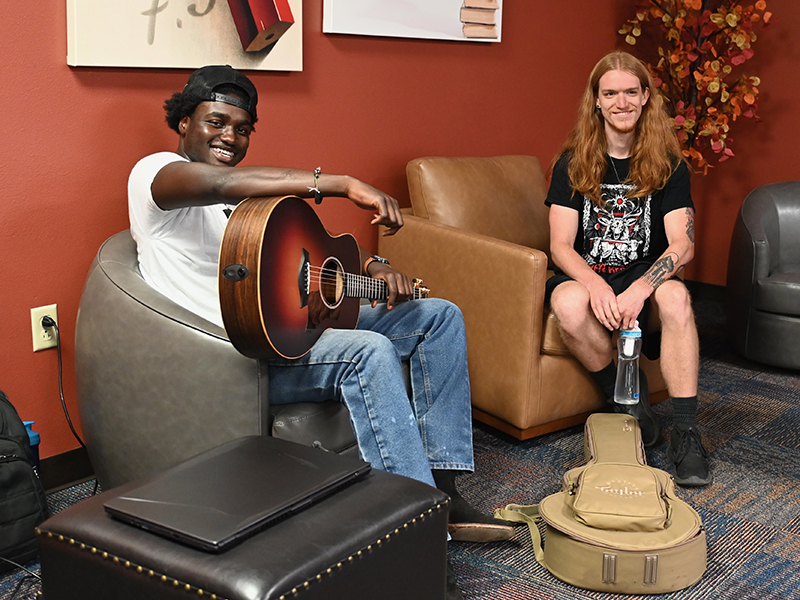 two-students-sitting-in-lounge-playing-guitar