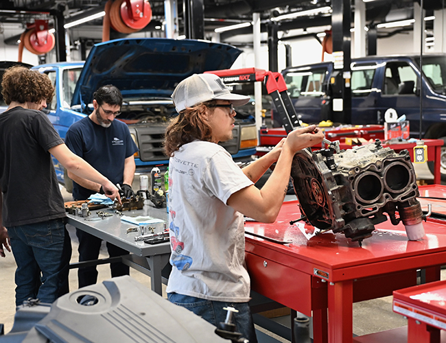 two students and instuctor working on engines