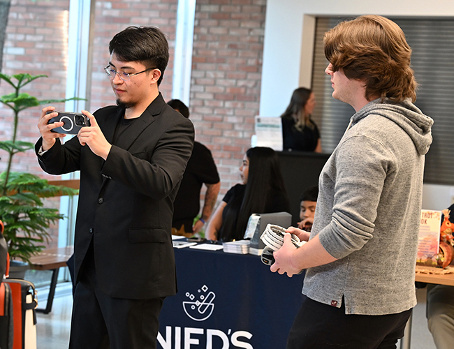 male student recording on camera and another student helping