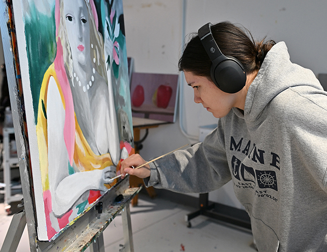female art student bending over painting on canvas